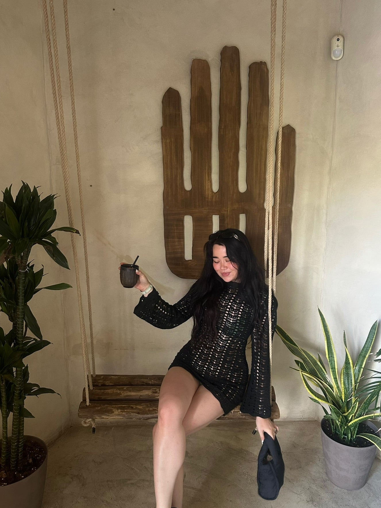 Woman in black outfit posing with a cactus-shaped wall decoration indoors holding a nylon puffer bag